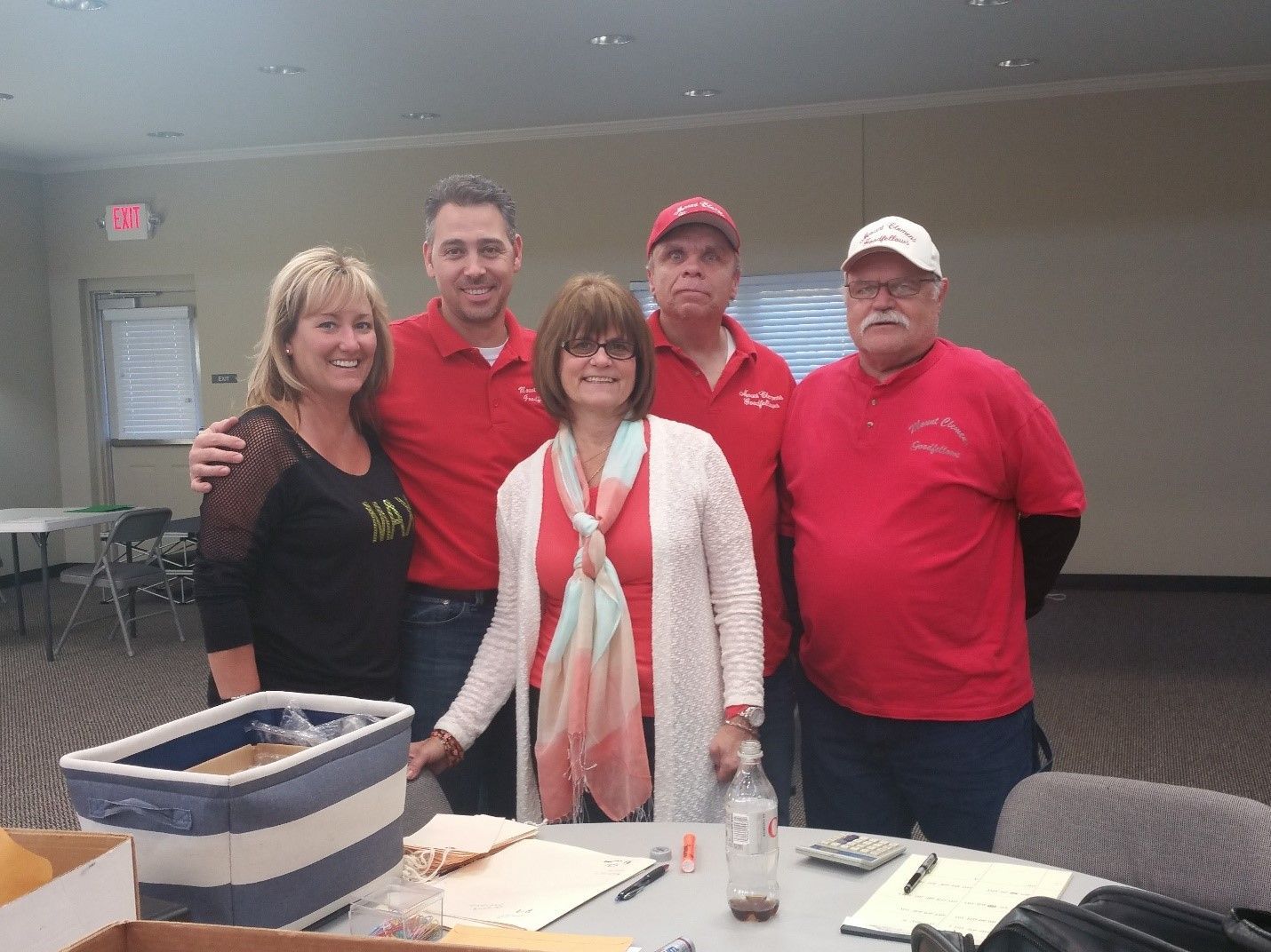 Five people in red shirts pose behind a table indoors.