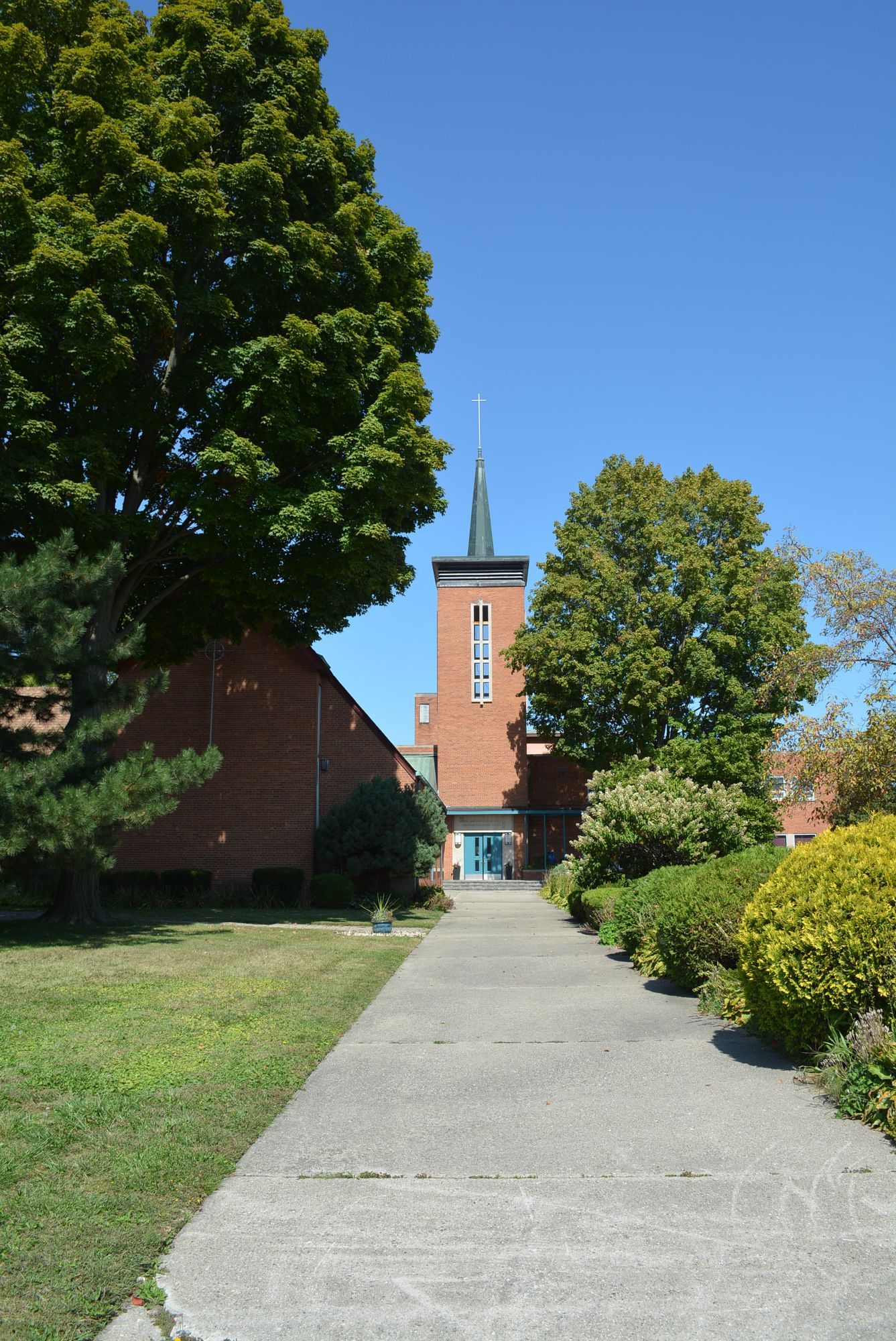 Paved pathway leads to a red brick church with a tall steeple on a sunny day.