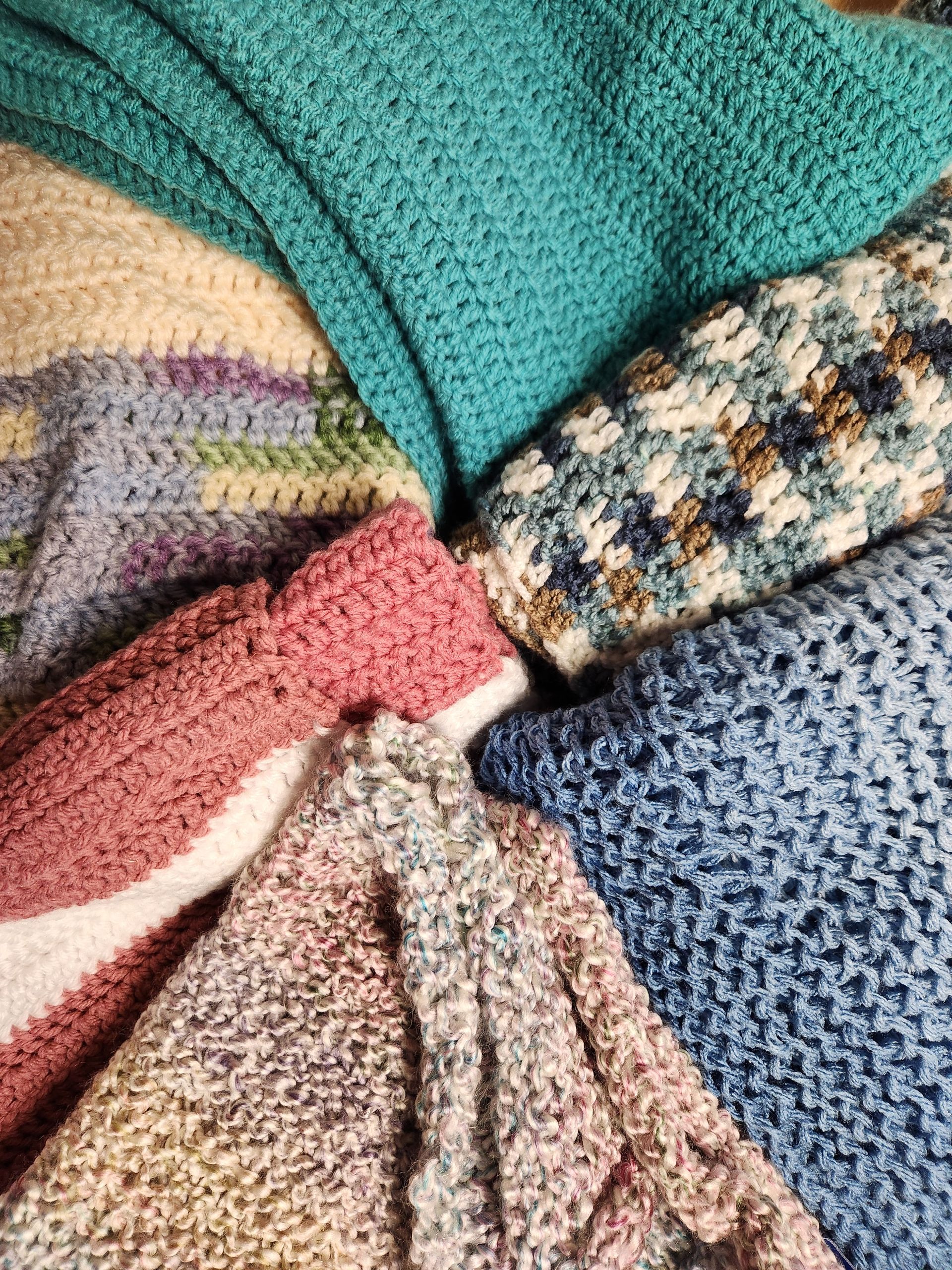 Close-up of a fan of textured crochet blankets in various colors: teal, cream, blue, pink, and multicolored.
