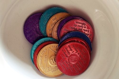 Colorful sobriety medallions in a white bowl, various colors and text.