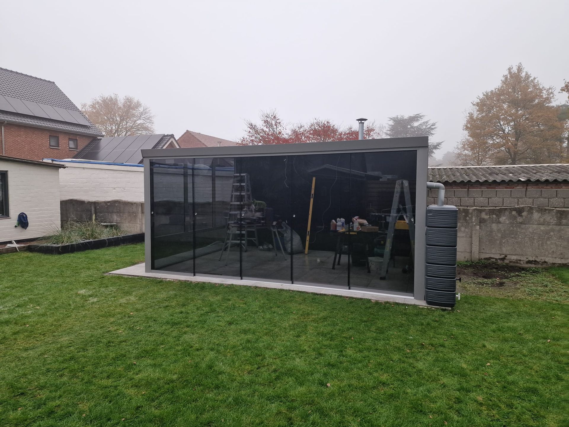 Klein zwart tuinhuisje of prieel met gaaswanden in een grasrijke achtertuin op een bewolkte dag.