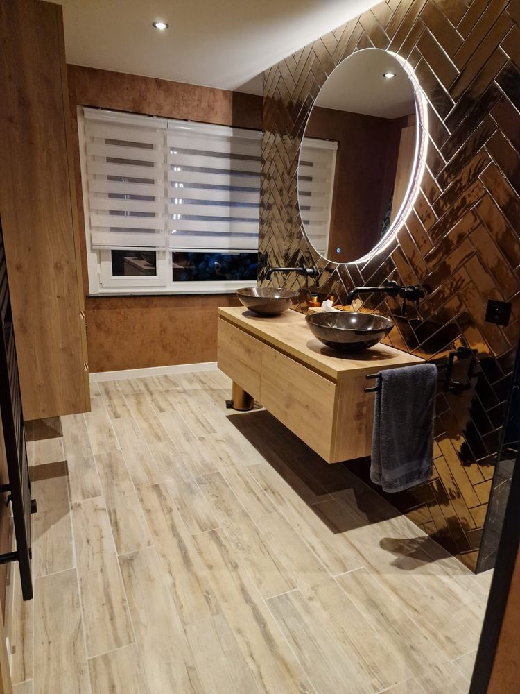 Moderne badkamer met houten lambrisering, een dubbele wastafel en een grote ronde spiegel met verlichting.
