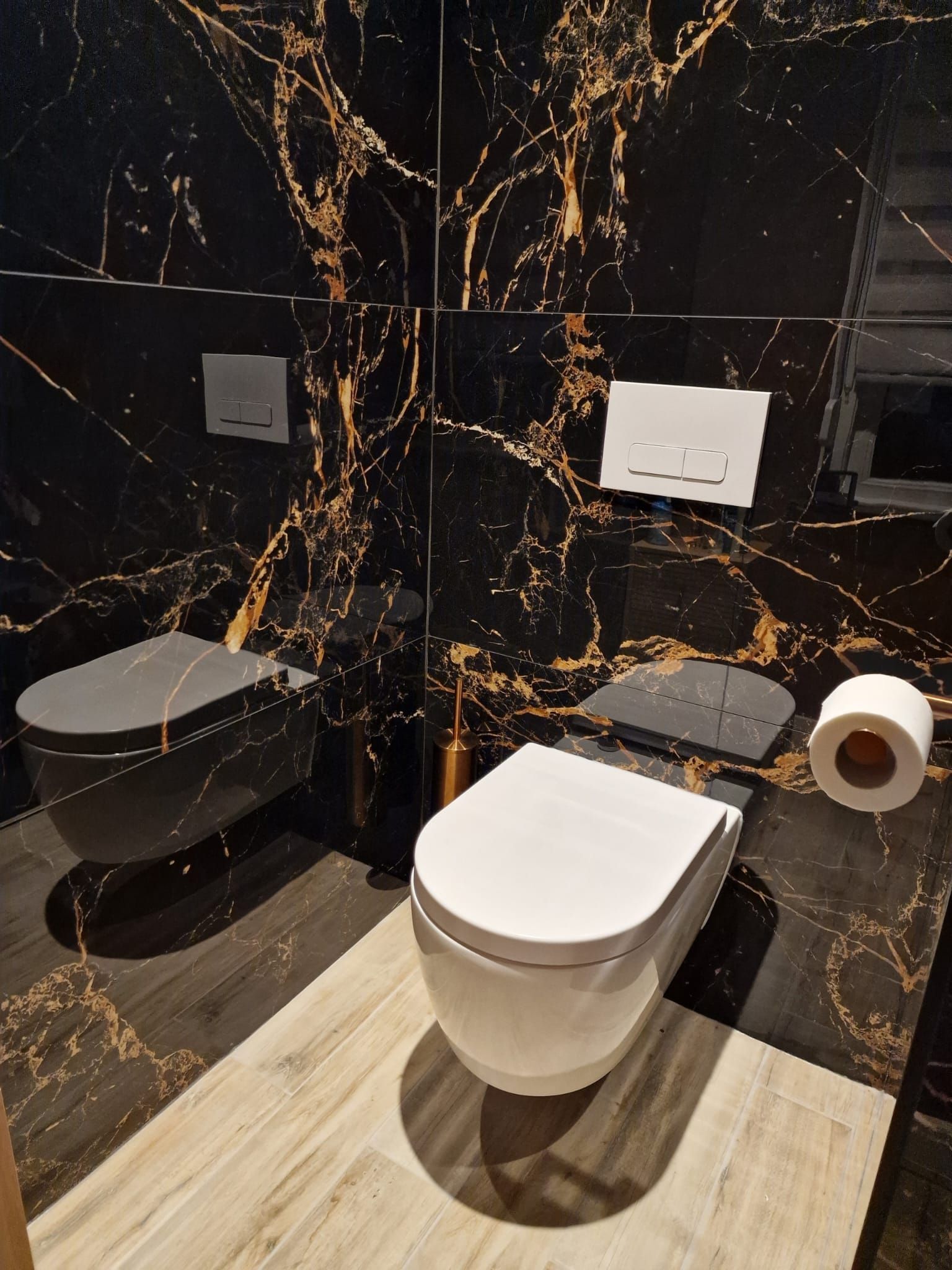 Moderne badkamer met zwarte marmeren muren, wit toilet en aan de muur gemonteerde wastafel met kranen.