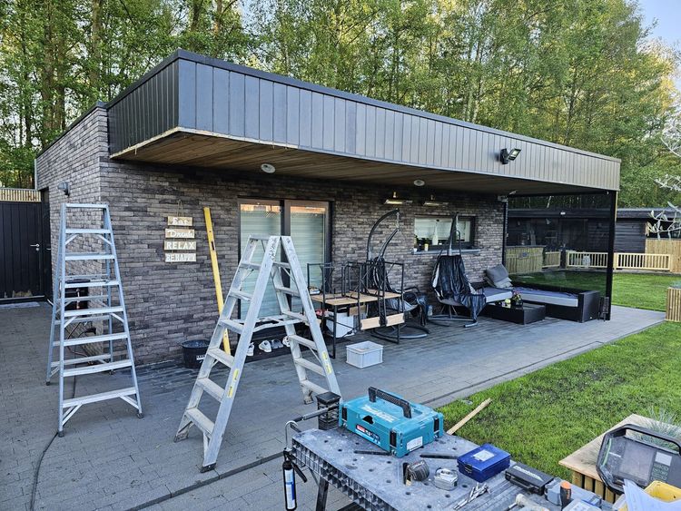 Terras met ladders en gereedschap naast een modern bakstenen en metalen gebouw in aanbouw.