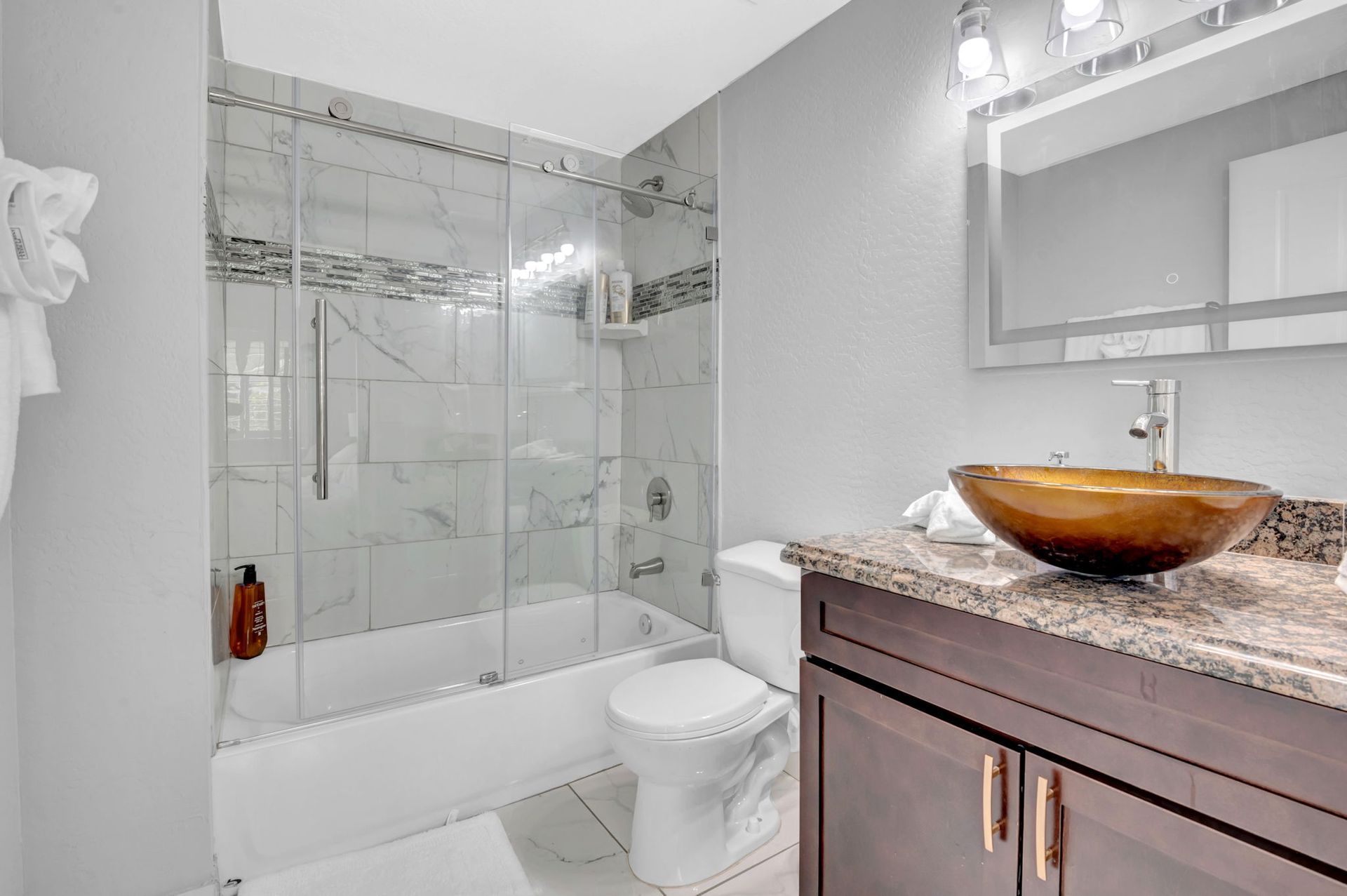 Bathroom with glass shower, brown sink, white toilet, gray walls, and mirror.