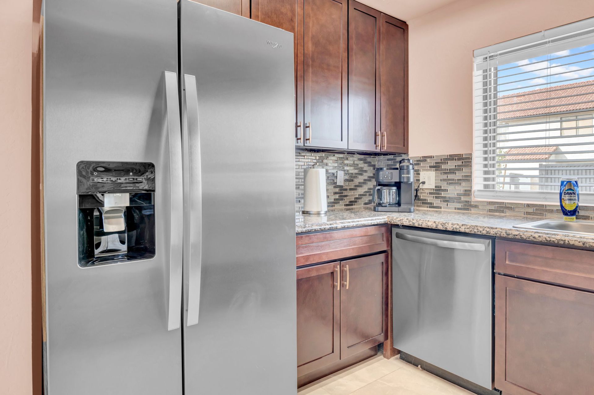Stainless steel refrigerator and kitchen cabinets in a kitchen with a window and countertop.