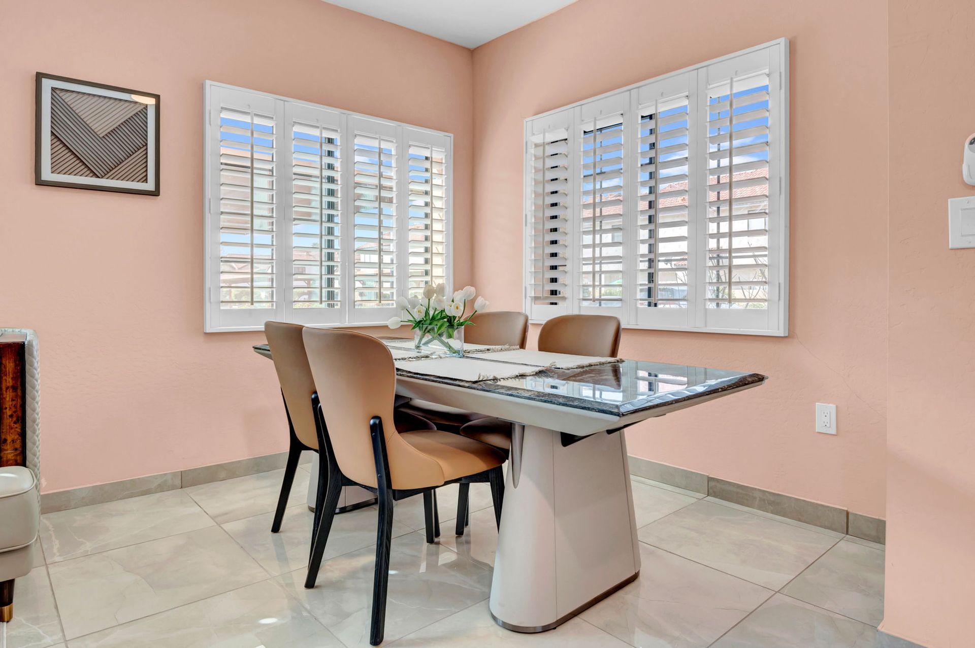 Dining room with pink walls, a table, chairs, and two shuttered windows.