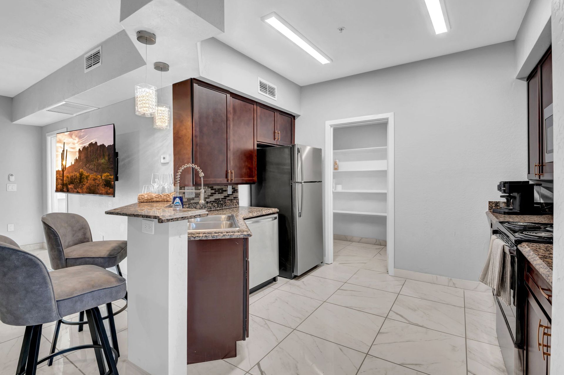 Modern kitchen with dark cabinetry, stainless steel appliances, and a breakfast bar with stools.
