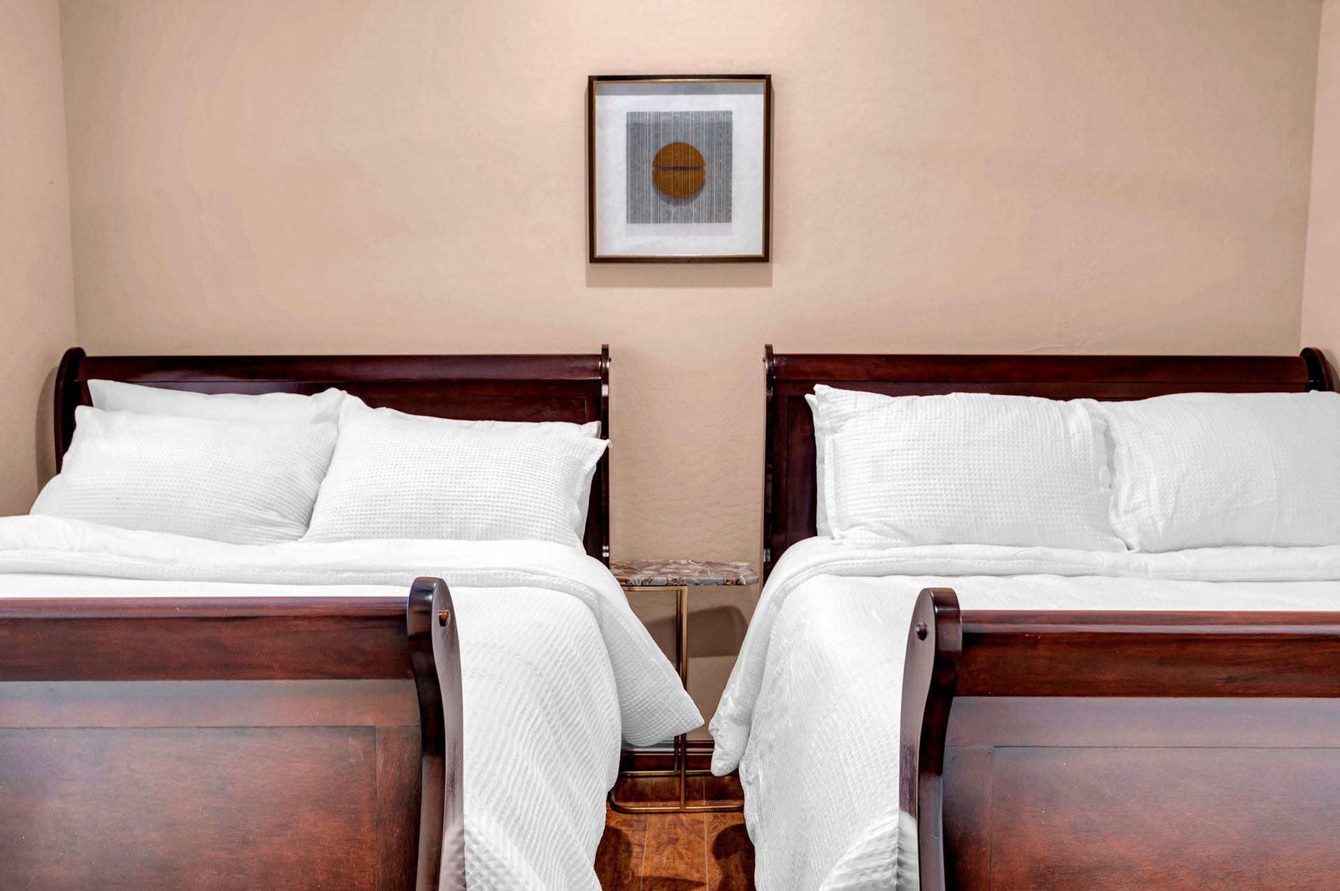 Two beds with white bedding, in a room with a framed art piece above a small nightstand.