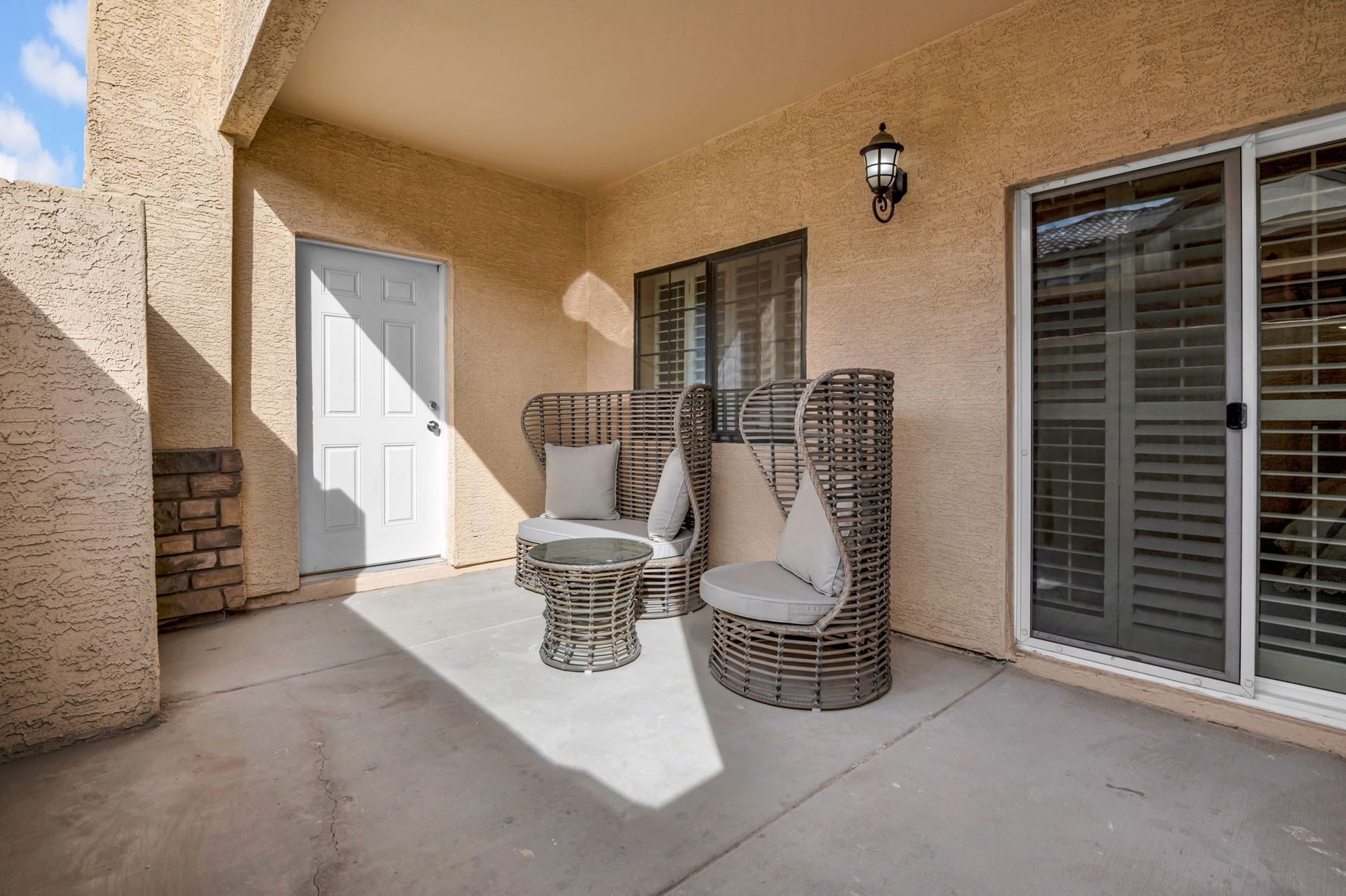 Covered patio with wicker seating, door, and sliding glass door.