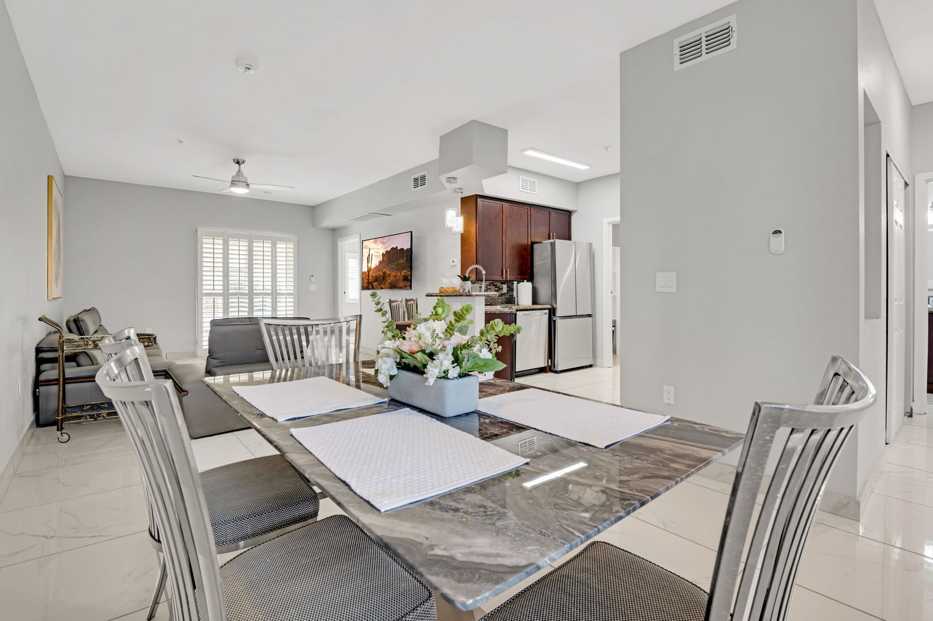 Open-concept dining and living space; marble table, chairs, kitchen in background.