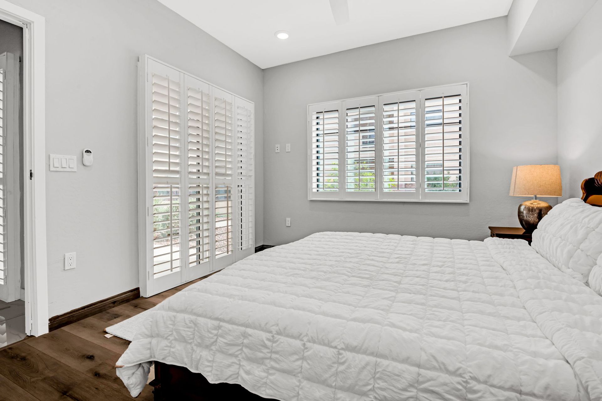 Bedroom with bed, shutters on windows and doorway, bedside table with lamp.
