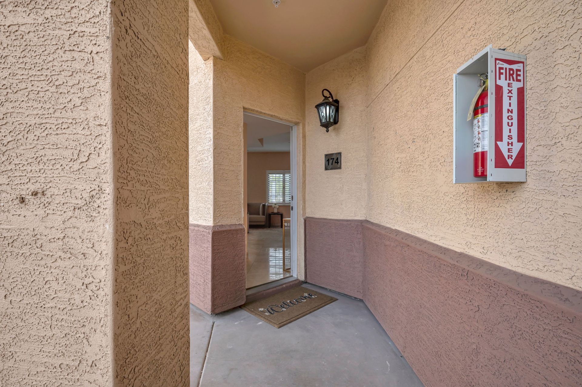 Entryway with textured beige and brown walls, open door, fire extinguisher.