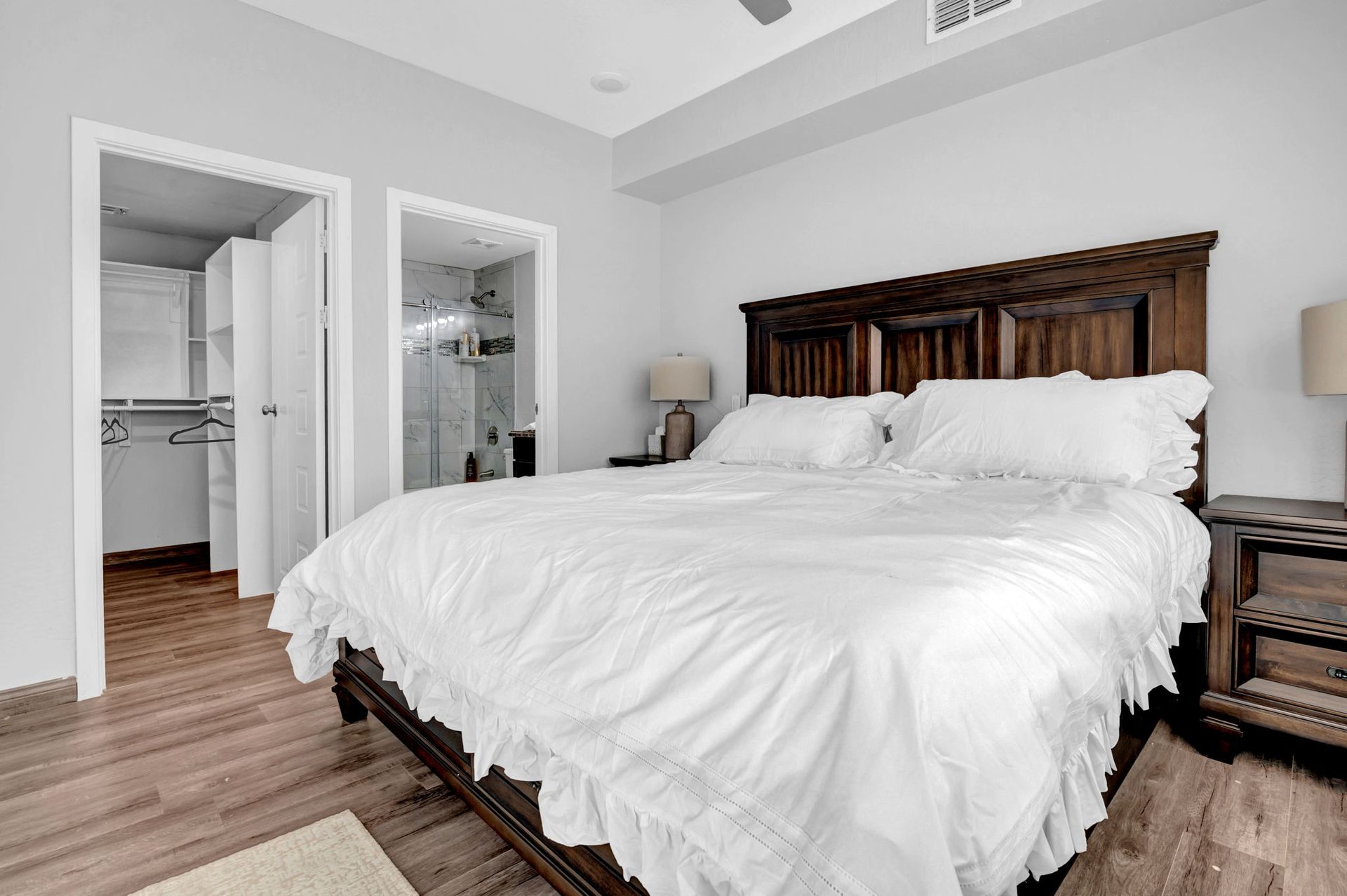 Bedroom with large wooden bed, white bedding, and two nightstands. Closets and a bathroom are visible.