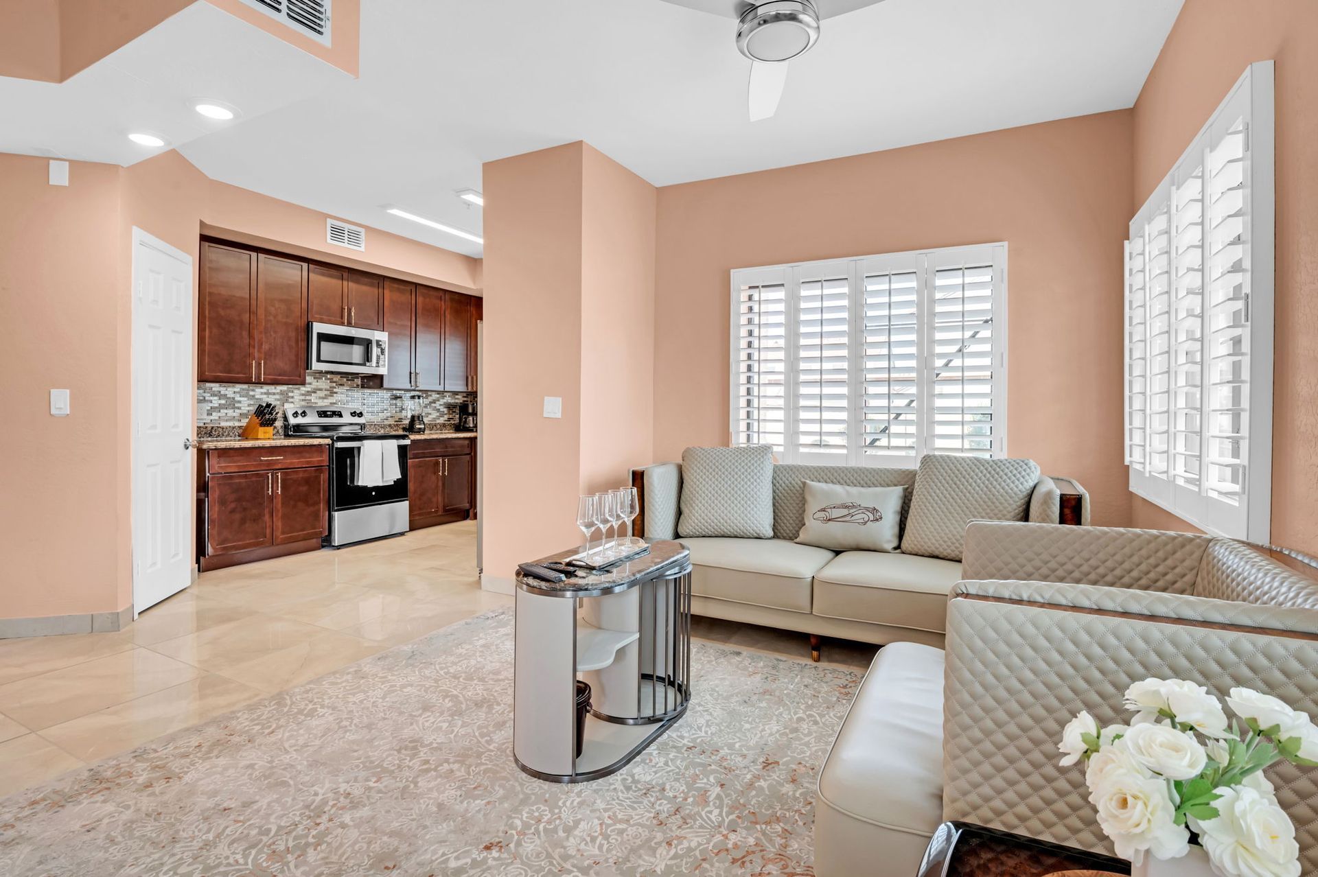 Living room with peach walls, beige couch, and kitchen in the background.