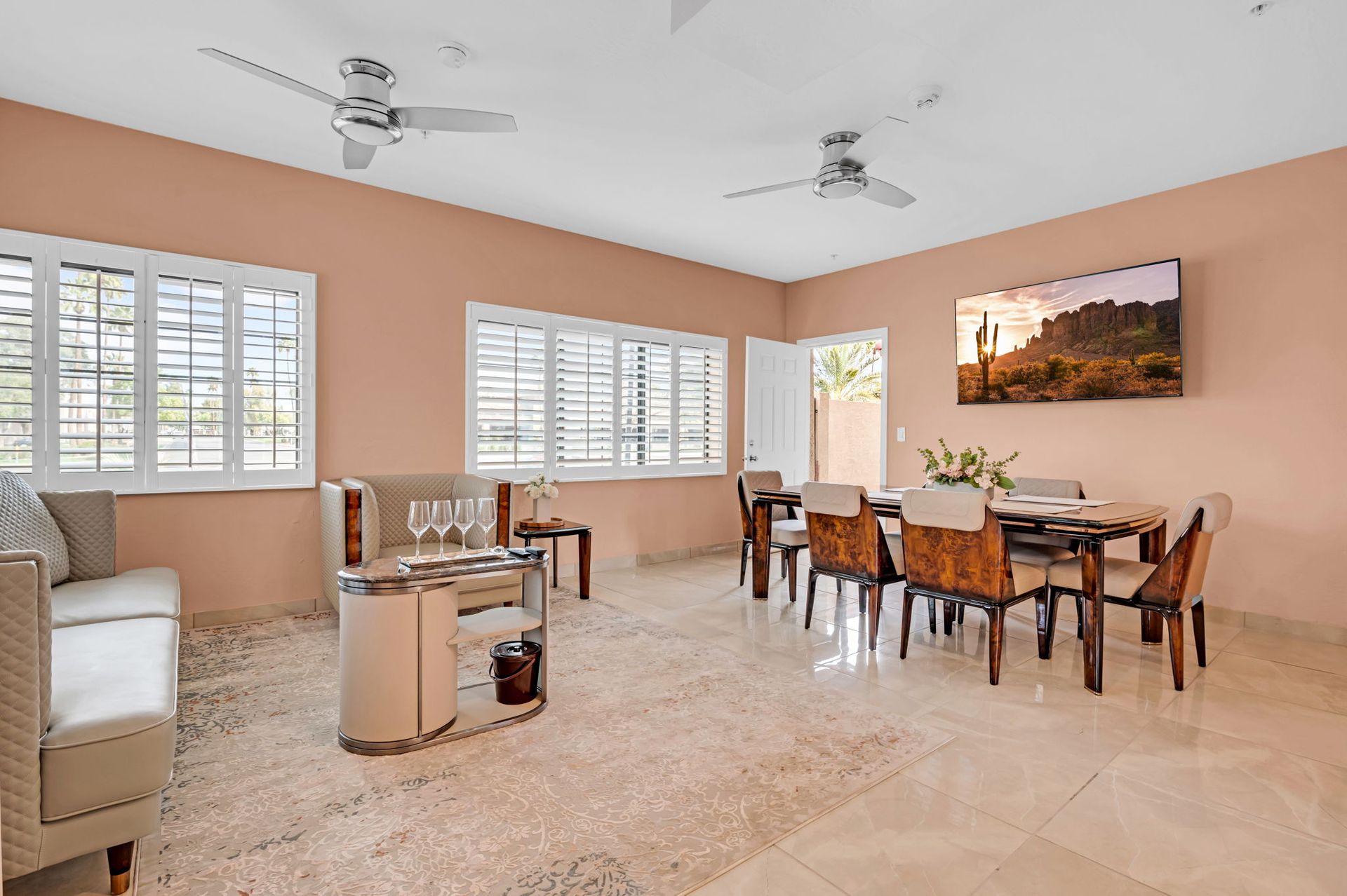 Spacious living and dining area with beige walls, large windows, ceiling fans, and a table set for dining.