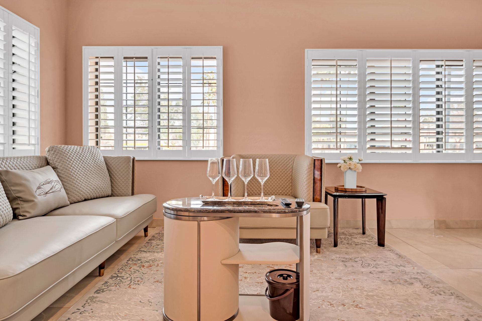 Living room with beige walls, white shutters, and a coffee table with wine glasses.