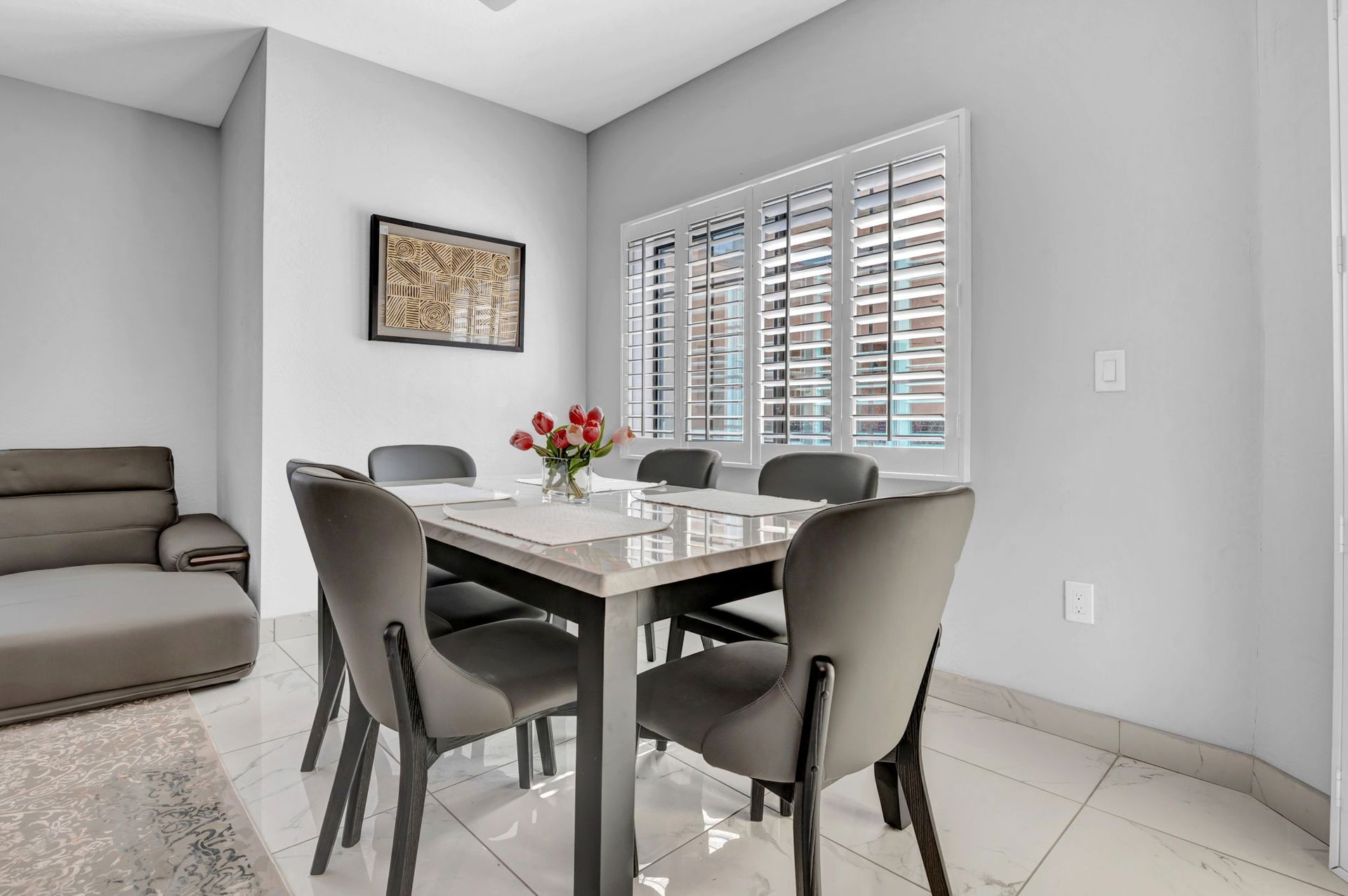 Dining room with a table, chairs, and a window. Gray walls and seating.