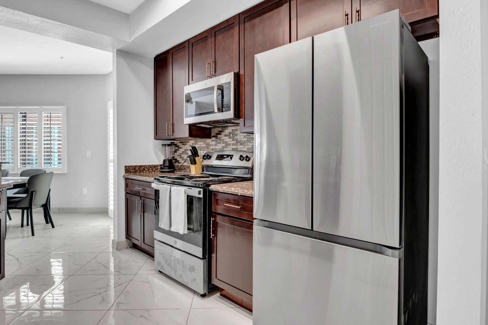 Kitchen with stainless steel refrigerator, dark wood cabinets, stove, microwave, and speckled countertop.