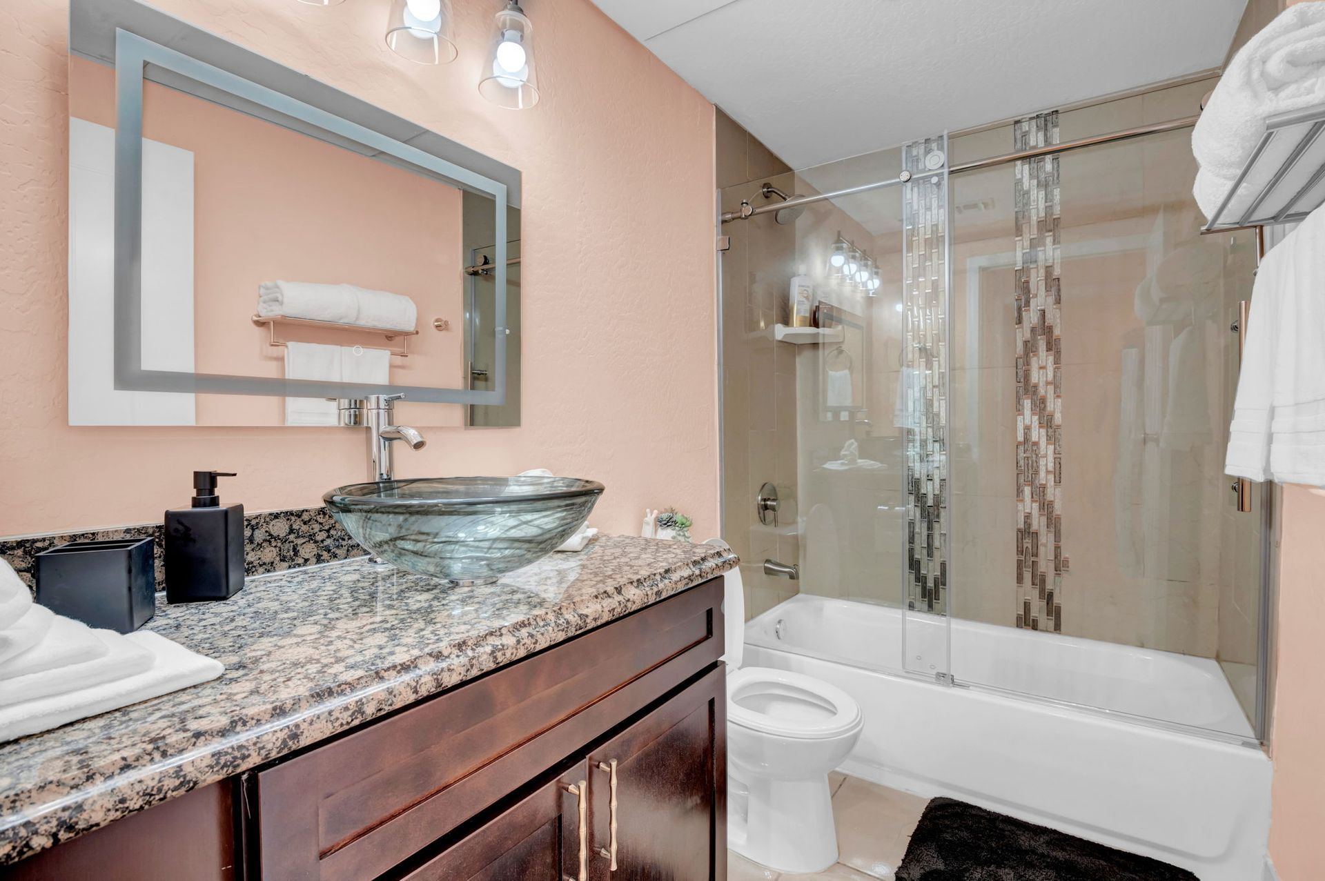 Bathroom with peach walls, dark vanity, glass sink, granite countertop, and shower with patterned curtain.