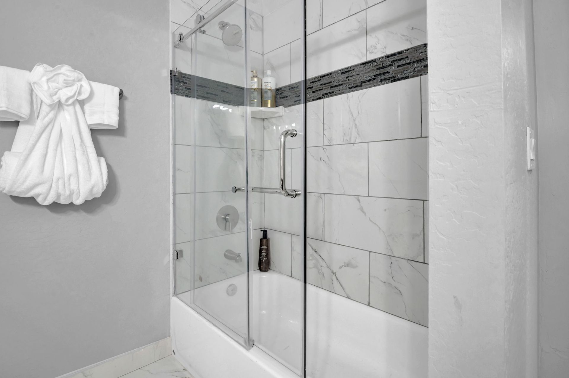 Bathroom with glass shower doors, white tile, and a towel arrangement.