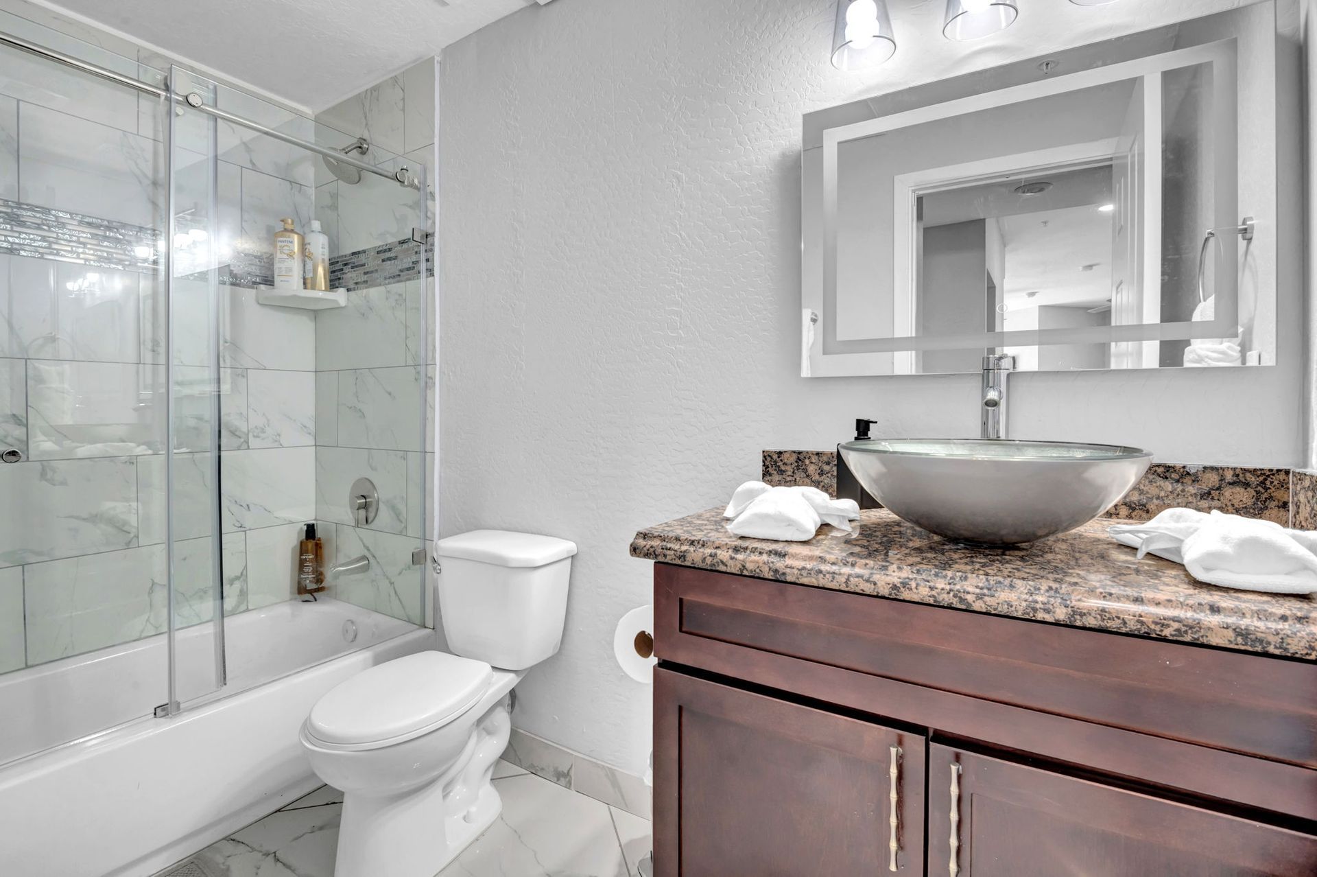 Bathroom with a white toilet, brown vanity, glass sink, and a shower/tub combo with glass doors.