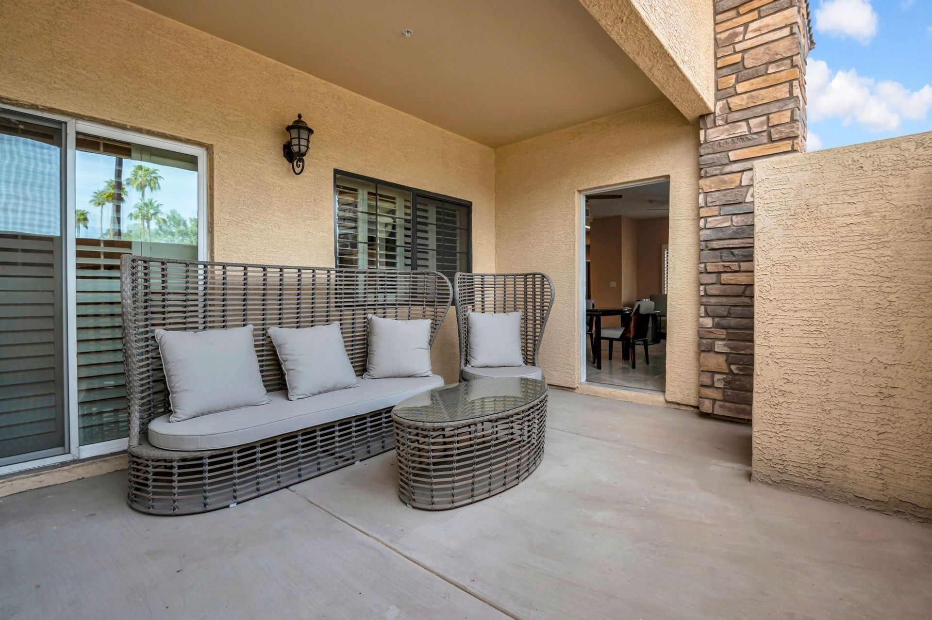 Patio with gray wicker sofa, glass-topped coffee table, and open doorway to dining room.