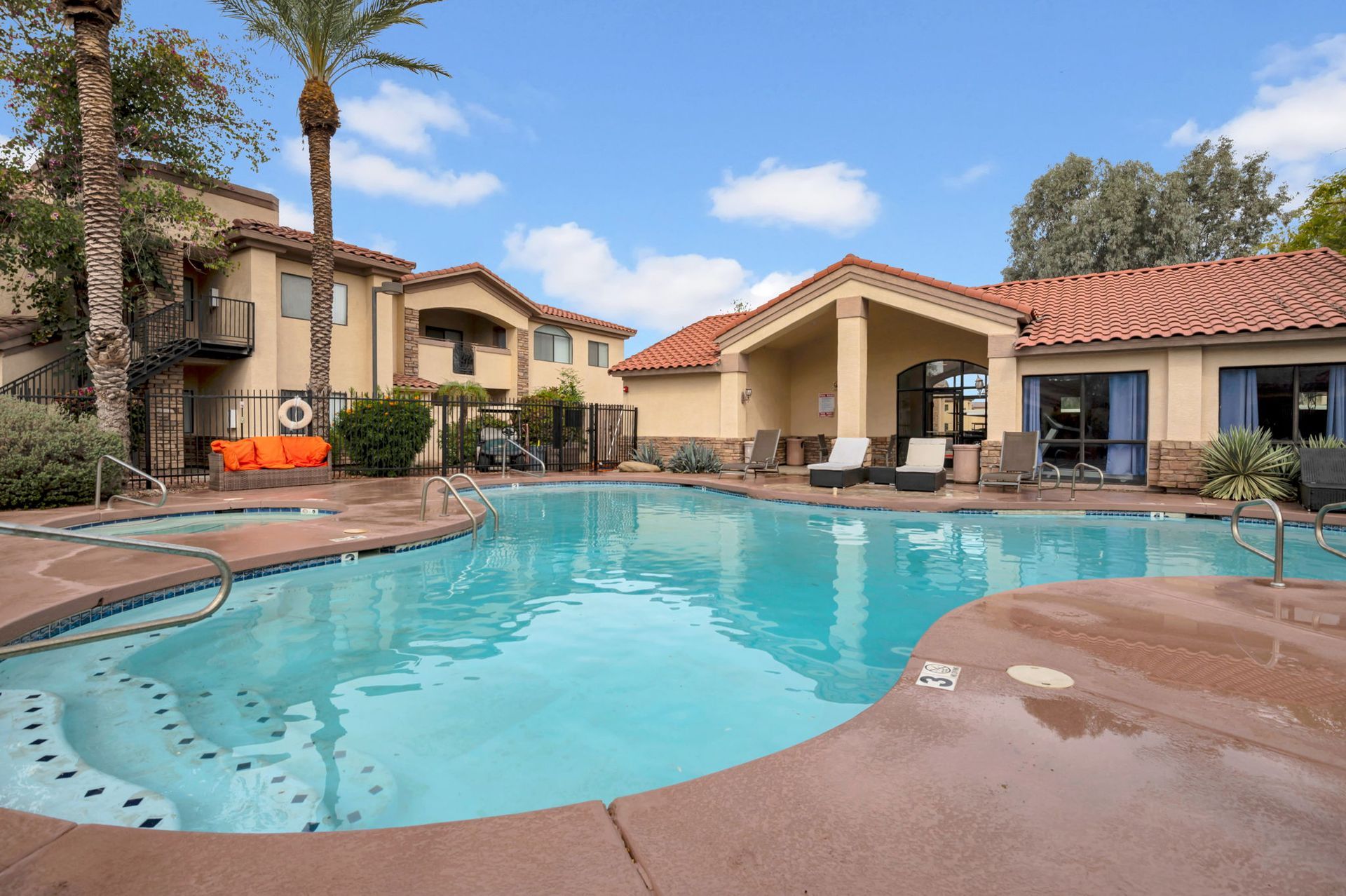 Swimming pool with lounge chairs next to a building with red tile roof under a blue sky.