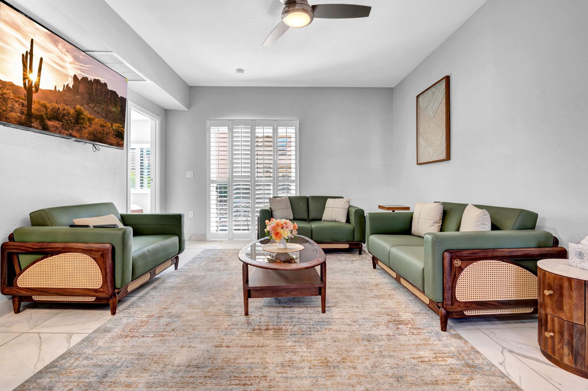 Living room with green sofas, a coffee table, and a large rug. A large landscape painting hangs on the wall.