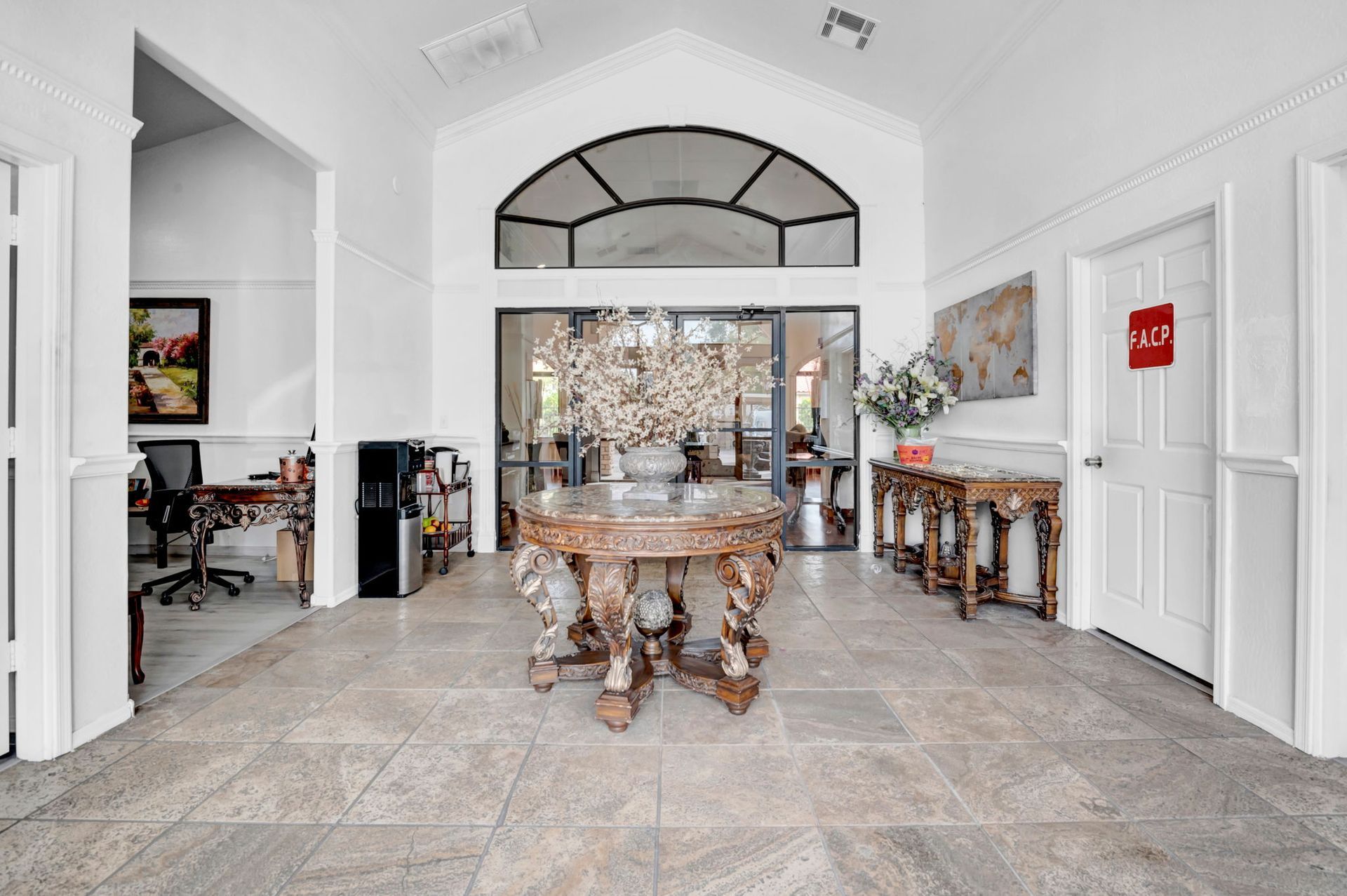 Grand entryway with carved wooden table, glass doors, and light-colored tiled floor.