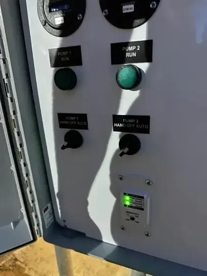 Electrical control panel with gauges, buttons, and a green indicator light in an open cabinet.