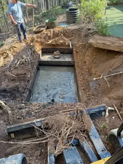 Excavation site with a concrete pit, dirt walls, and a worker standing nearby amidst exposed roots and debris