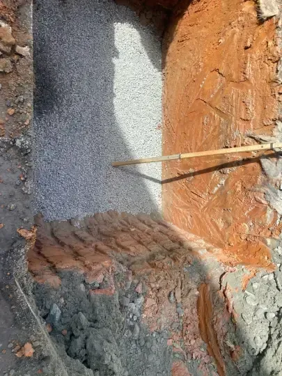 Cross-section of a trench with exposed orange soil, gray gravel, and two wooden stakes
