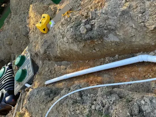 White pipe and cable laid along a rocky dirt slope with yellow and green utility items.