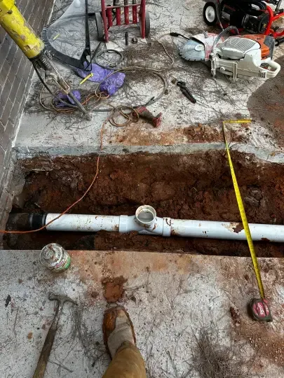 Trench excavation with exposed white PVC piping, muddy ground, and scattered tools at a construction site