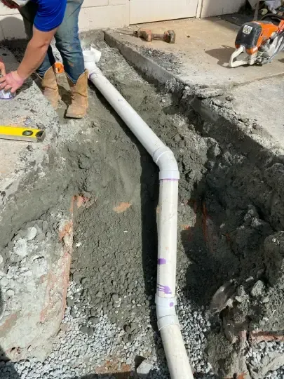 Workers install a white PVC pipe in a concrete trench during a construction project.