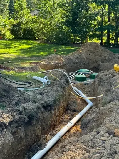 Trenches with white pipes and green utility lids in a grassy yard near trees