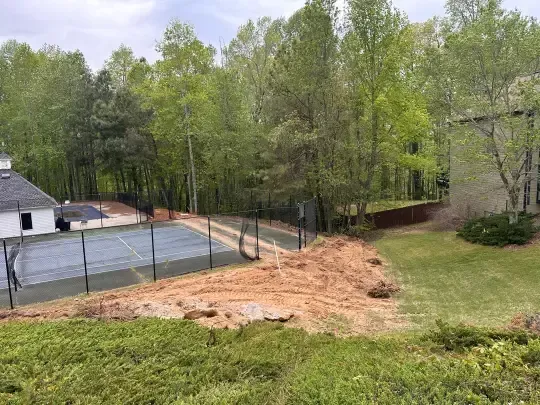 Backyard with fenced pool area, dirt excavation, grassy lawn, and trees in spring