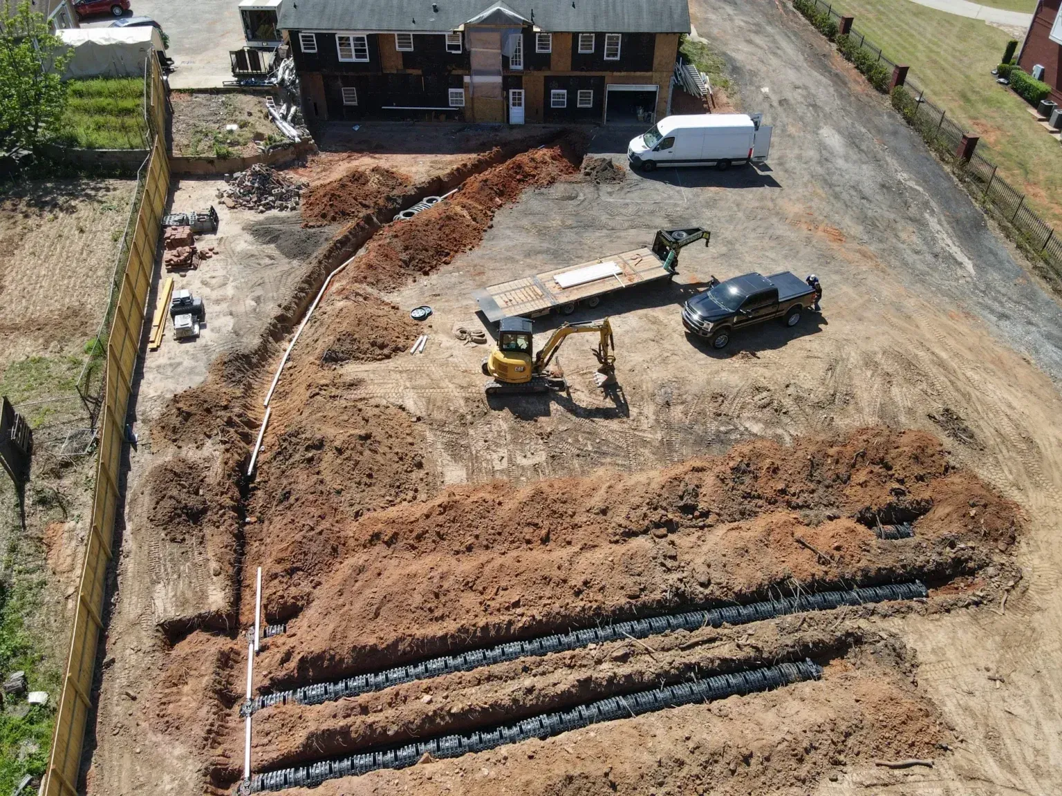 Aerial view of a house lot with excavator, truck, and long trenches dug in the dirt