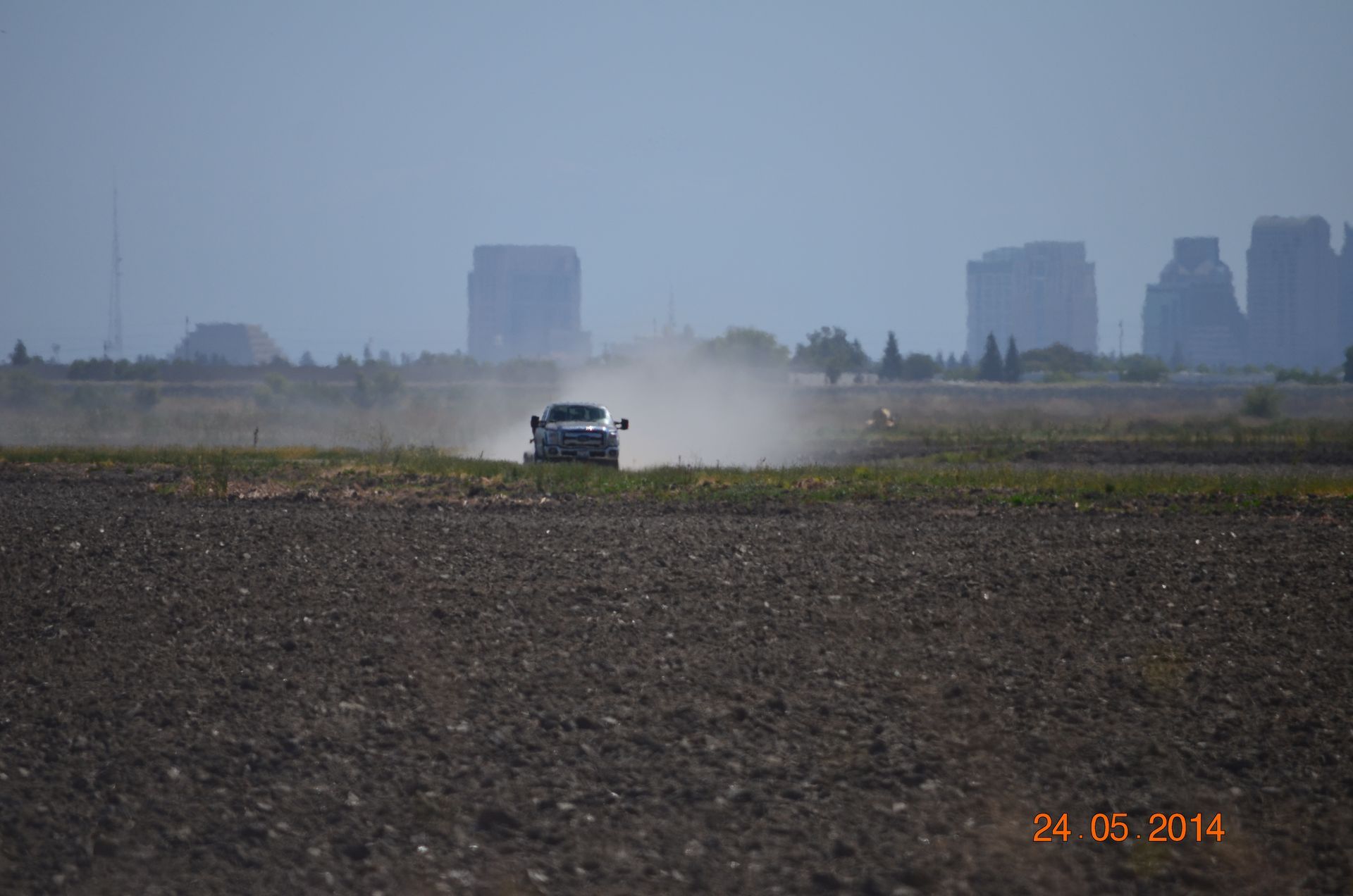 Car driving across a dusty field with city buildings in the hazy background