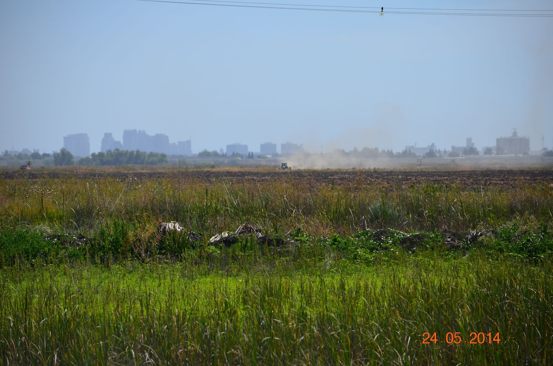 Wide grassy field with distant city skyline under a hazy blue sky