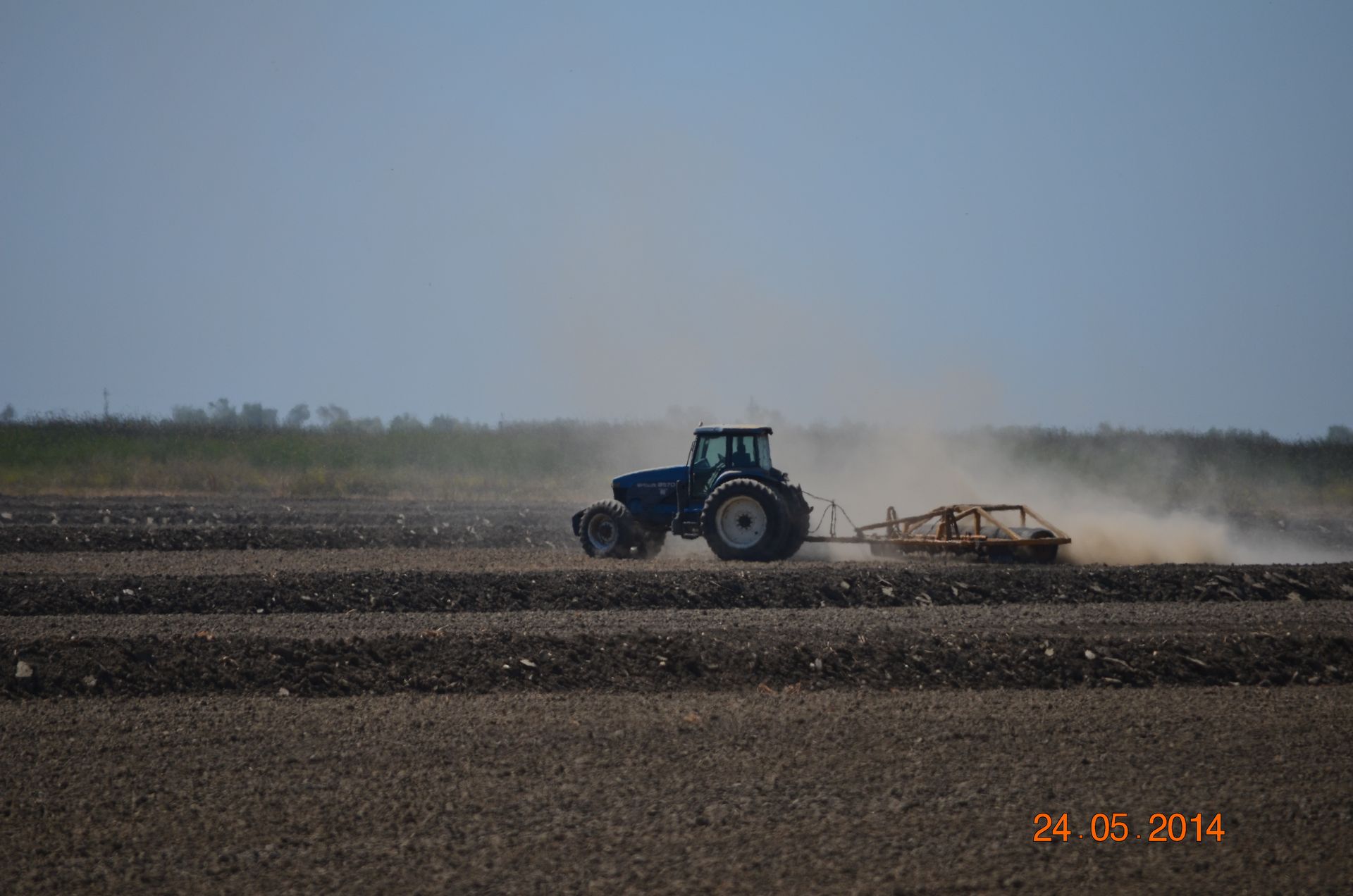 Blue tractor plowing a dusty field under a clear sky
