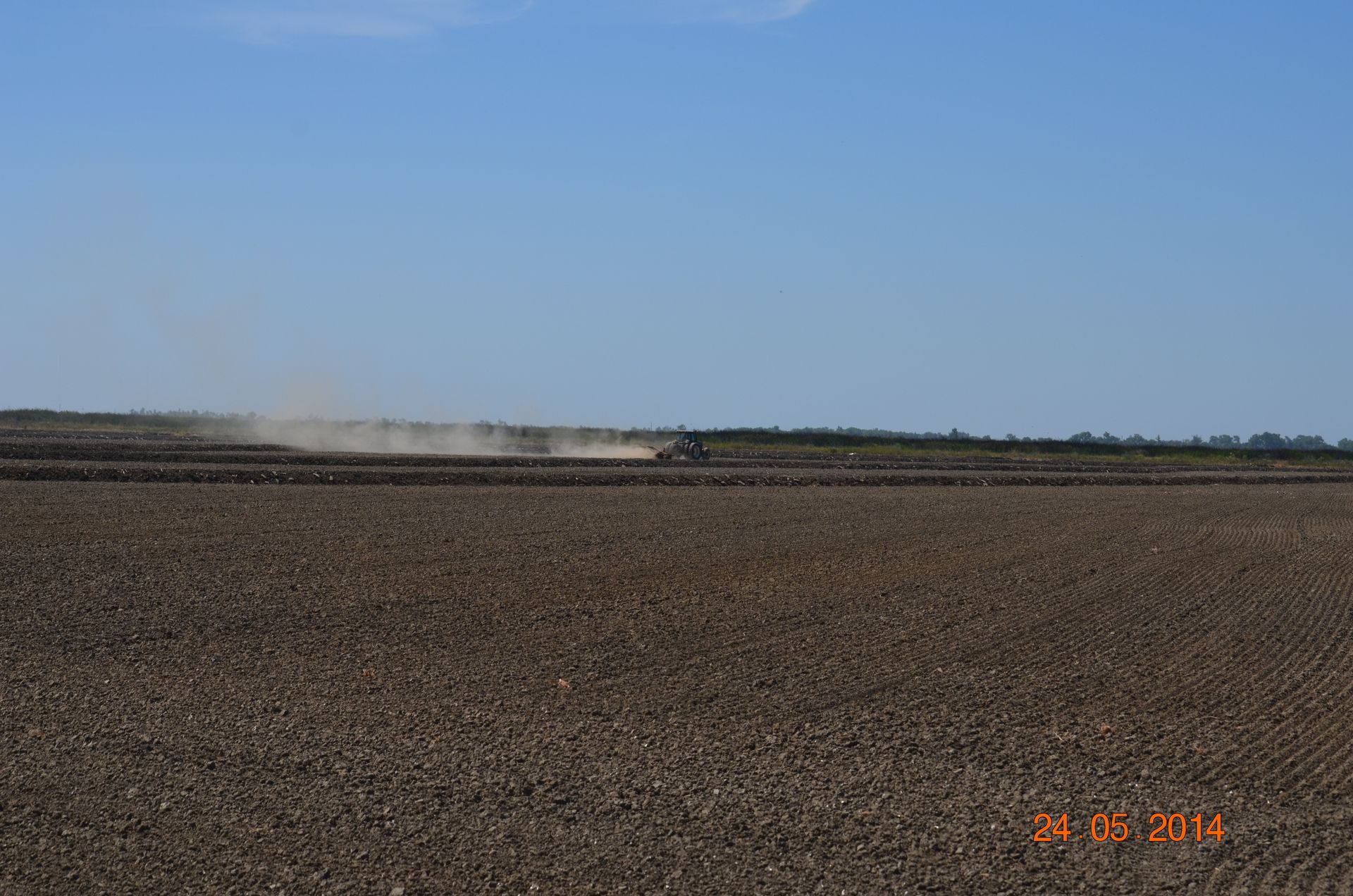 Open field under a blue sky with a faint dust plume on the horizon
