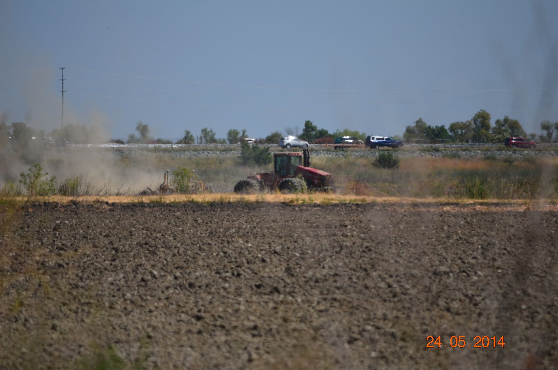Tractor plowing a dry field, kicking up dust under a clear sky.