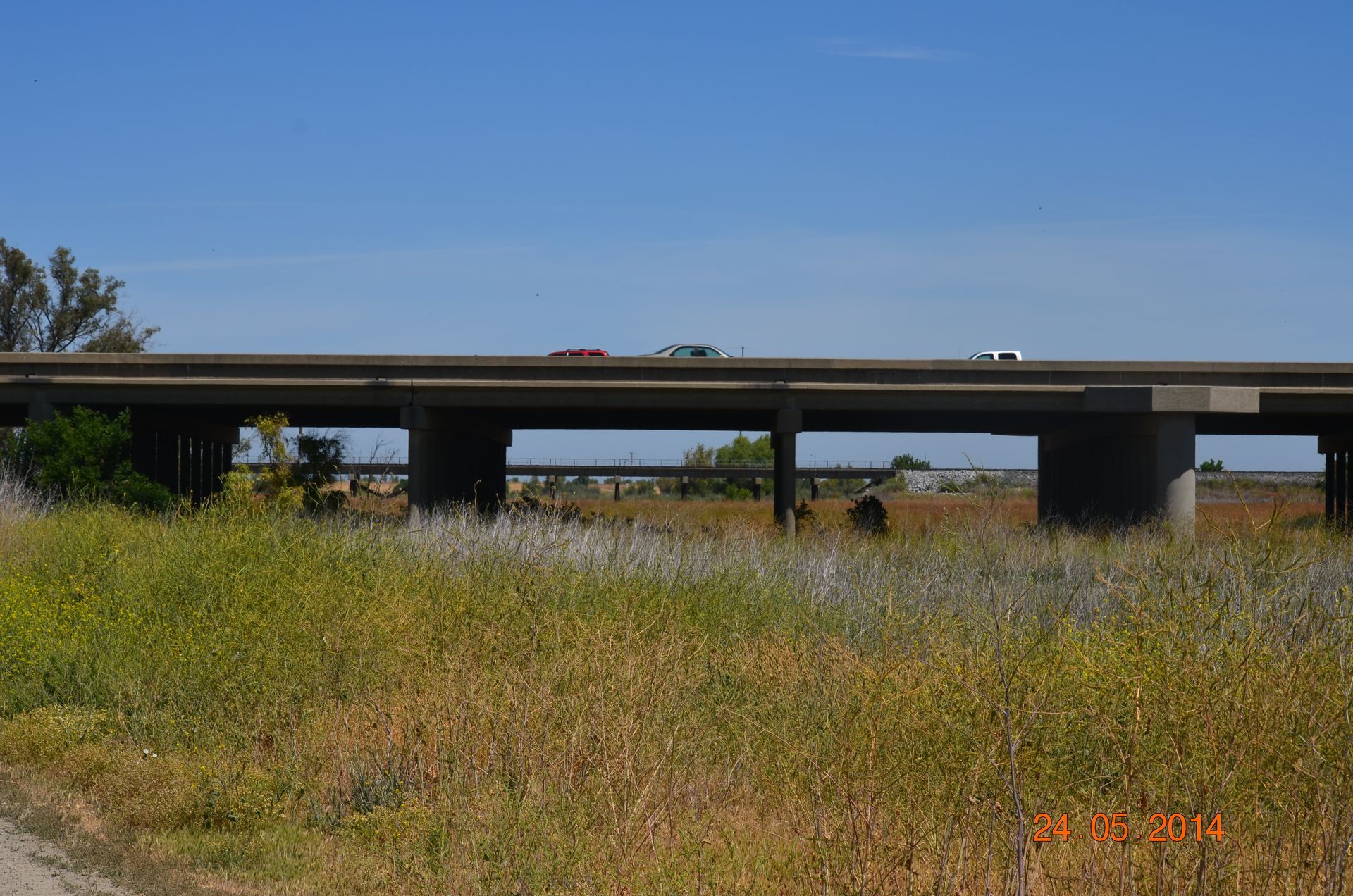 Highway overpass above dry grassy field under a clear blue sky