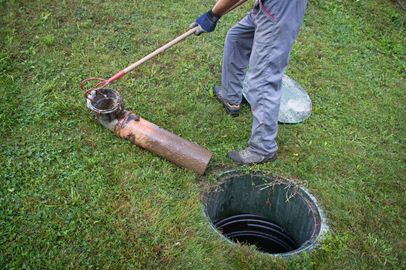 Worker using a tool to lift a pipe from a grassy yard beside an open manhole