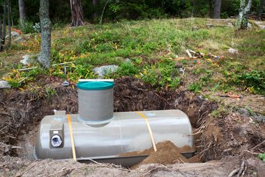 Gray underground tank with a teal vent cap installed in a wooded dirt clearing