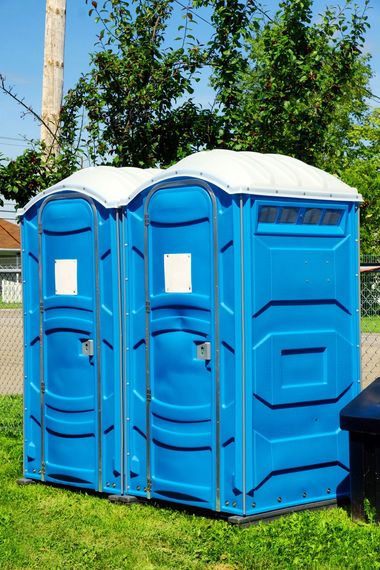 Three blue portable toilets standing on grass outdoors, with white roofs and trees behind them