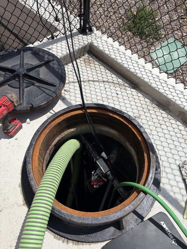Open manhole with green hose and cable on a rooftop behind a wire fence