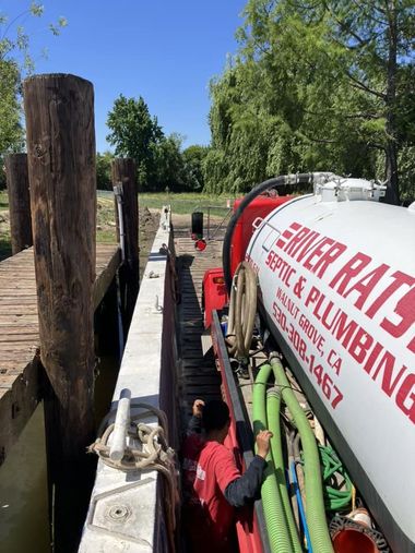 Red vacuum truck pumping sludge through a hose into a ground pit in a courtyard